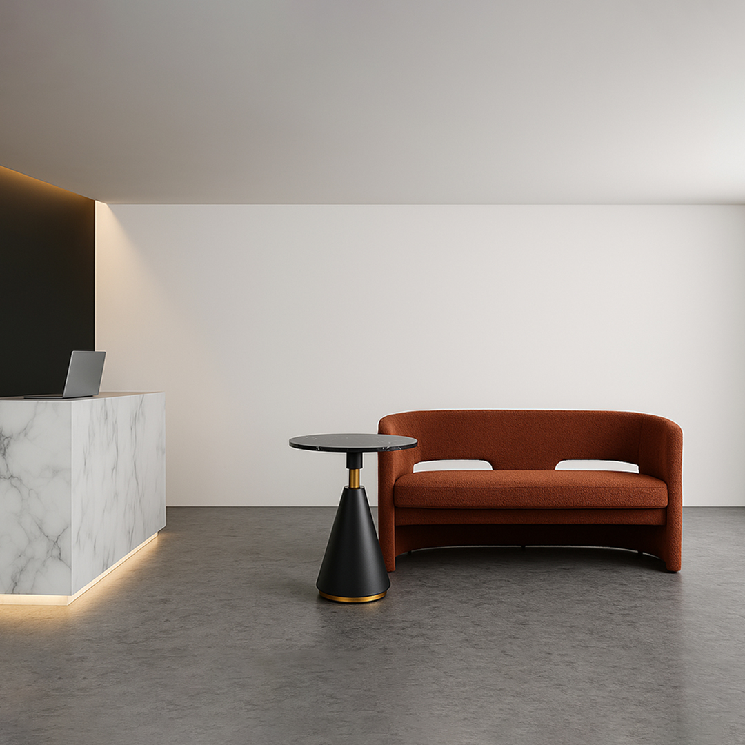Modern interior with a sleek marble reception desk on the left, a round black side table, and a rust-colored sofa on the right. Minimalist and calm.