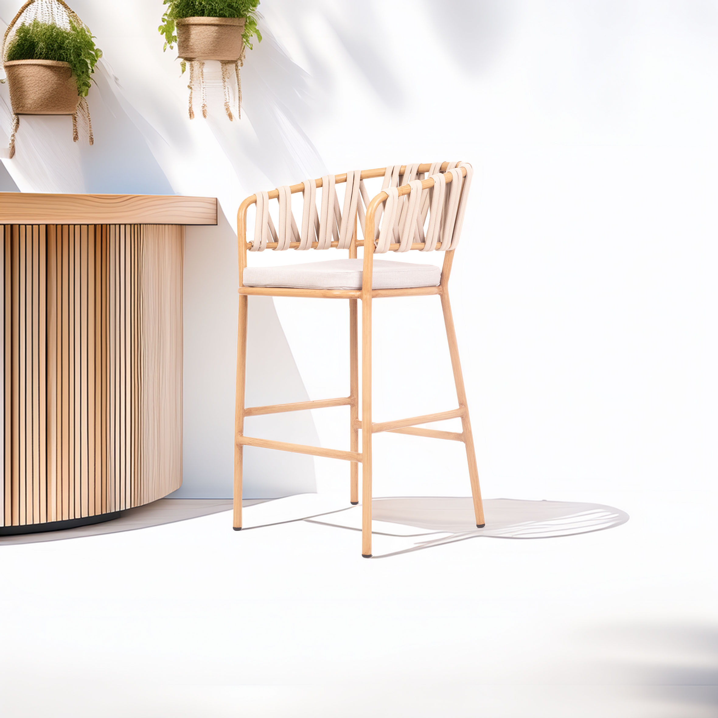 A light wooden bar stool with a woven backrest stands beside a wooden counter. The scene is bright and airy, with hanging plants casting soft shadows.