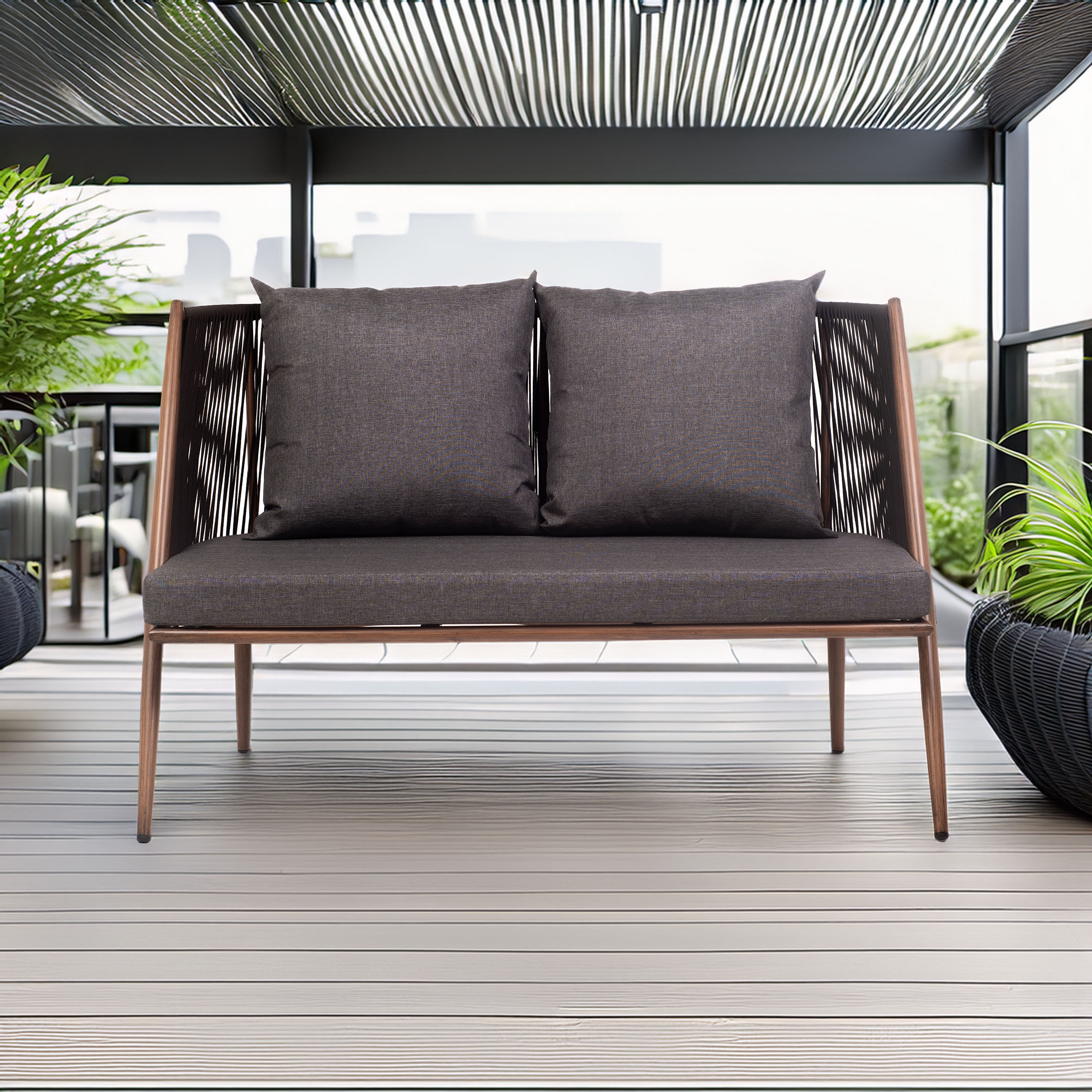A modern outdoor loveseat with dark cushions and a sleek wooden frame sits on a light deck. Surrounded by lush potted plants, it conveys a serene, elegant ambiance.