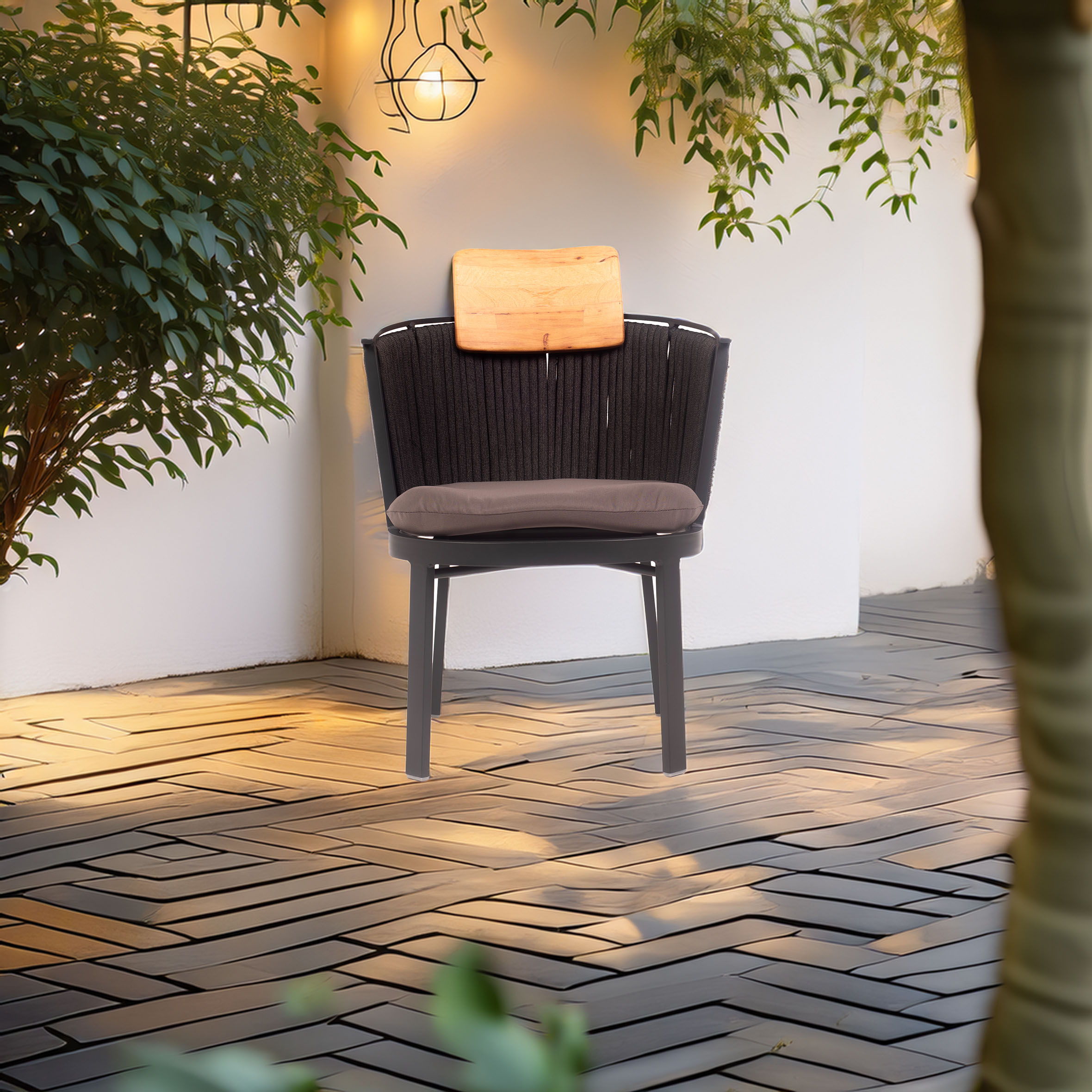 A cozy patio scene with a black wicker chair, wood accents, and a cushion placed on a patterned deck. Warm ambient lighting and lush green plants create a serene atmosphere.