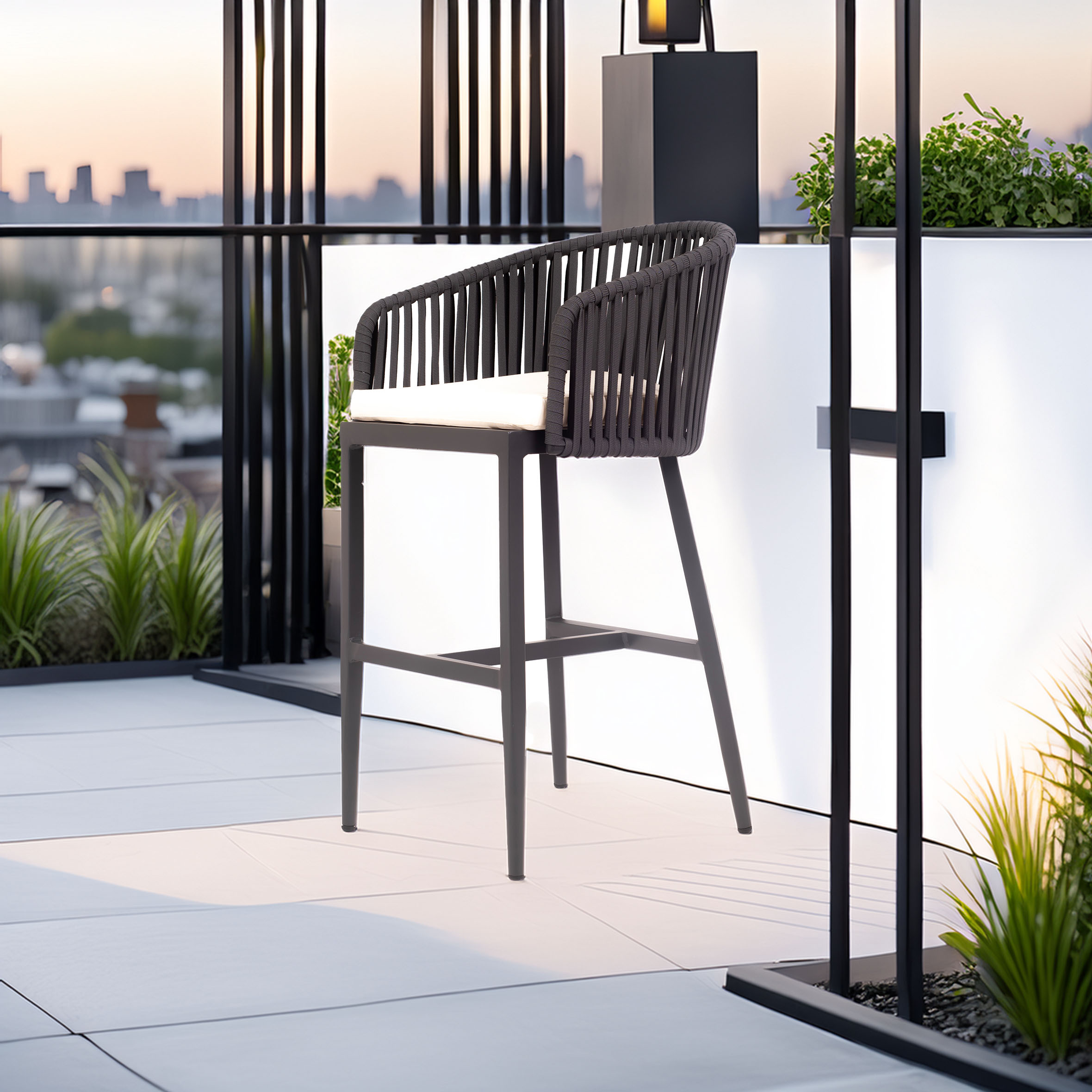 A modern rooftop patio at sunset features a sleek black bar stool with a woven backrest. Potted plants and a city skyline create a serene ambiance.