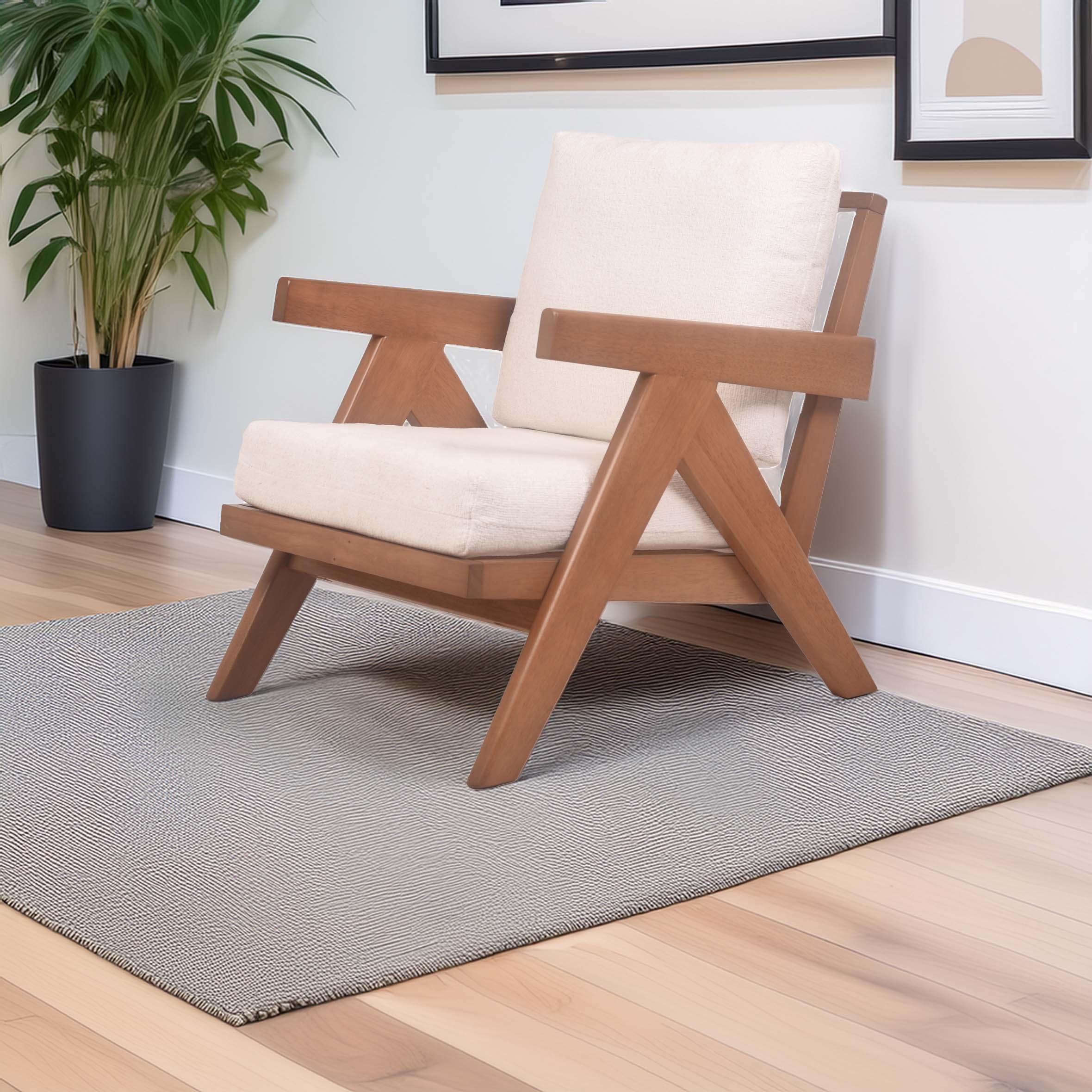 A modern wooden armchair with cream cushions sits on a textured gray rug. A green potted plant and framed artwork adorn the minimalistic room.