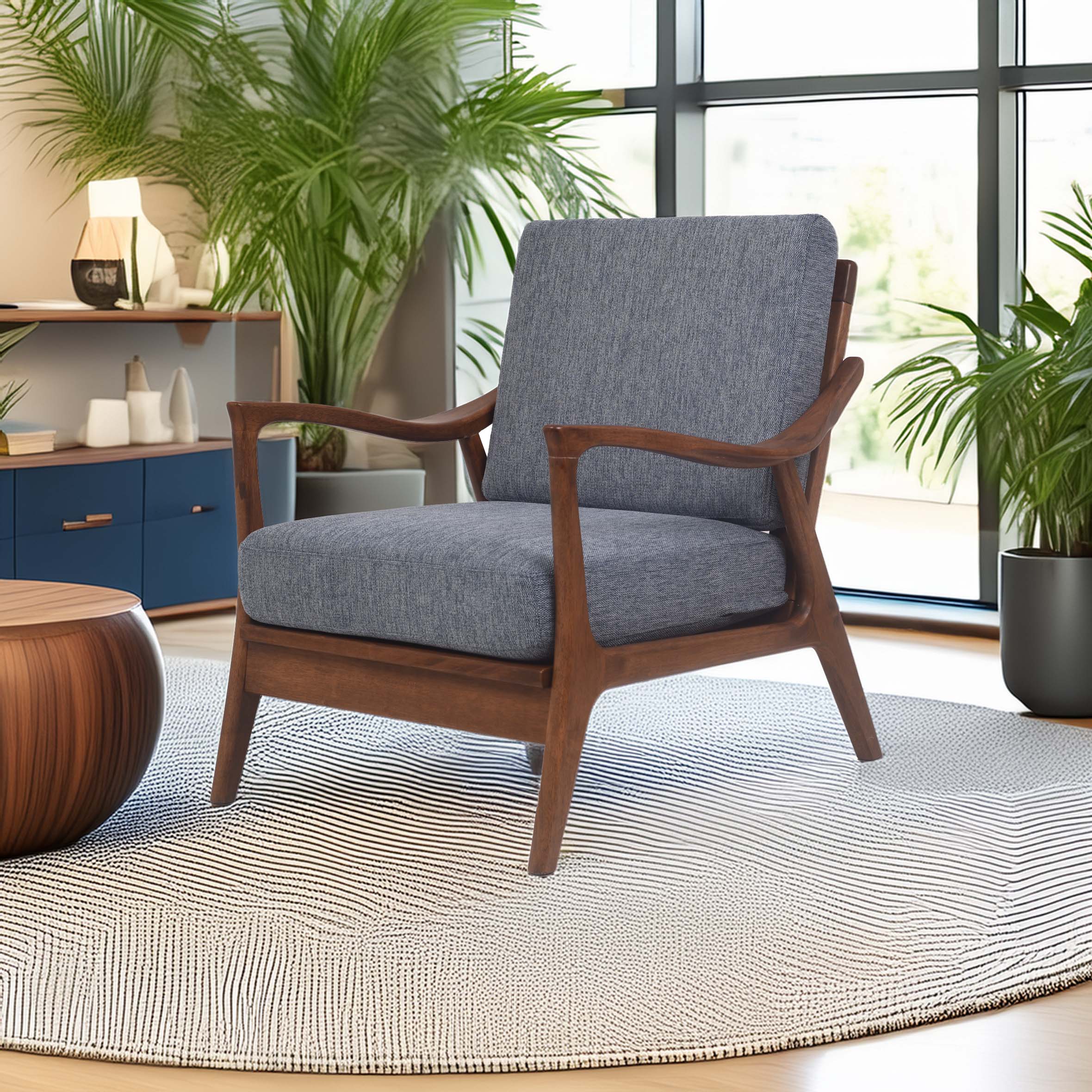 A modern living room with a mid-century armchair featuring gray cushions and wooden arms, set on a round, textured rug. Plants and soft lighting add a cozy feel.